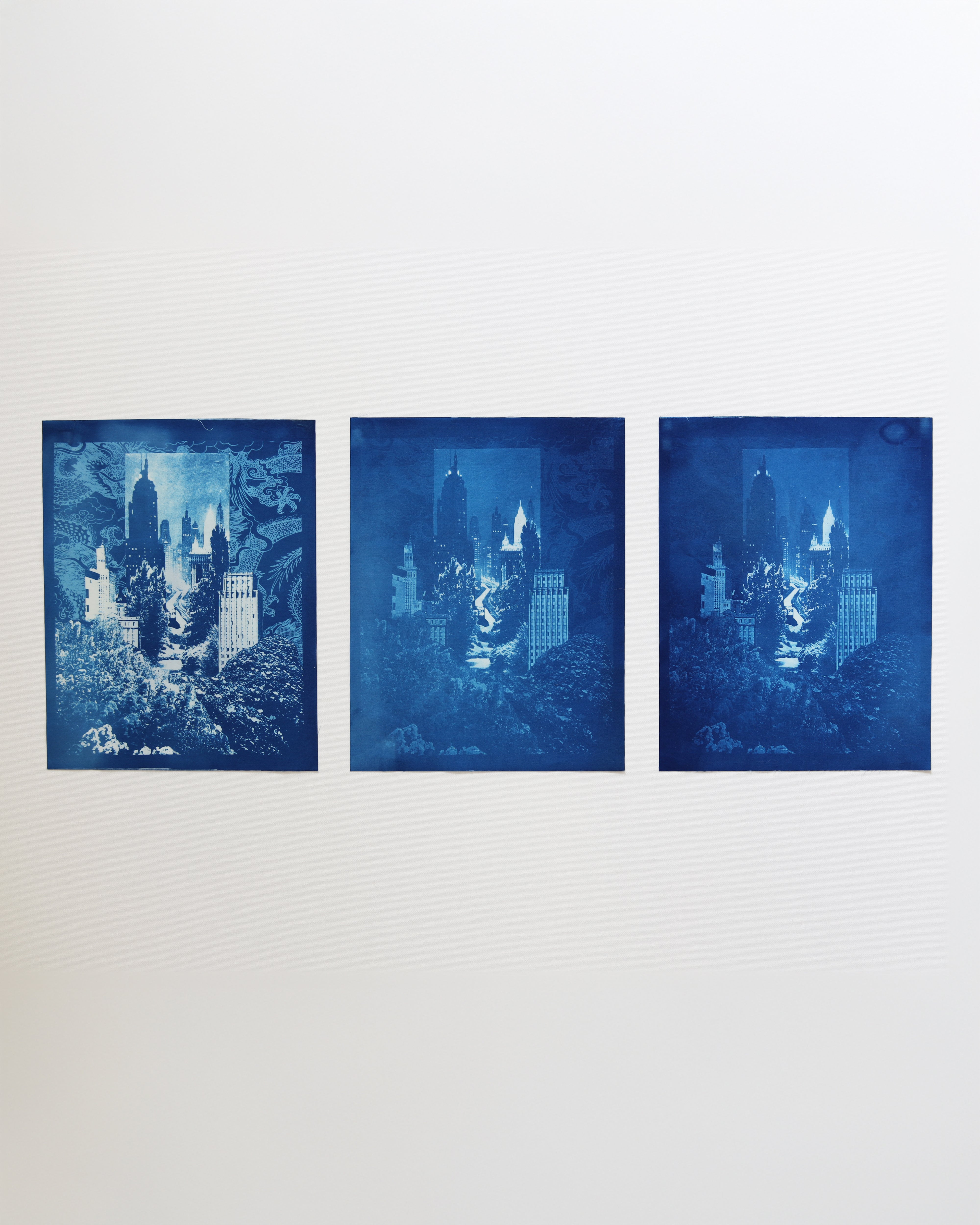 Three blue-toned prints of cityscapes on a white wall
